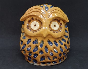 May include: A ceramic owl figurine with brown and blue glaze. The owl has large, round eyes and a detailed beak.