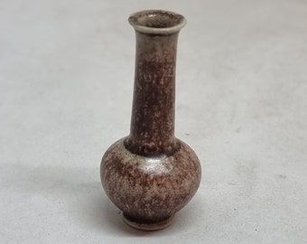 Puede incluir: Un pequeño jarrón de cerámica marrón y blanco con cuerpo redondeado y cuello estrecho.