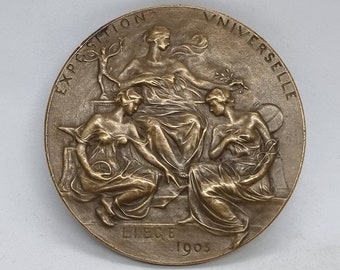 Könnte beinhalten: Bronzemedaille zur Erinnerung an die Weltausstellung 1900 in Paris. Die Medaille zeigt drei Frauen, eine sitzend und zwei stehend, mit der Inschrift "Exposition Universelle" am Rand und "Liege 1900" unten.