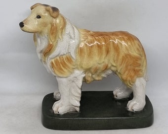 May include: A ceramic figurine of a brown and white Collie dog standing on a black base.