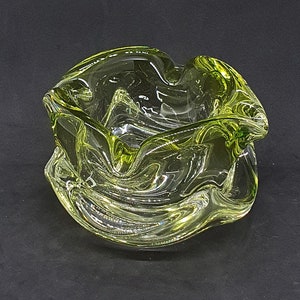Puede incluir: Un cuenco de vidrio verde con un diseño ondulado y orgánico. El cuenco está hecho de vidrio transparente con un tinte verde.
