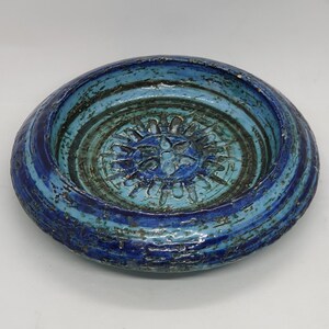 May include: A blue and green ceramic dish with a circular design in the center. The dish has a textured surface and a slightly raised rim.