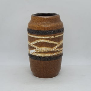 Puede incluir: Un jarrón de cerámica marrón con un patrón geométrico blanco y marrón. El jarrón tiene una base redondeada y una forma cilíndrica.