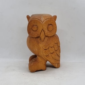 Könnte beinhalten: Eine Holzfigur eines Eulen mit brauner Oberfläche. Die Eule hat große Augen und detaillierte Federn.