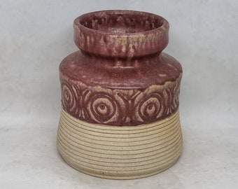 May include: A ceramic vase with a brown and white glaze. The vase has a wide base and a narrow neck. The top of the vase is decorated with a pattern of circles.