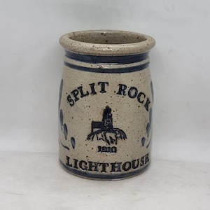 Könnte beinhalten: Eine weiße Keramikdose mit blauen und schwarzen Details. Die Dose zeigt eine Leuchtturm-Illustration und den Text "Split Rock Lighthouse 1910".