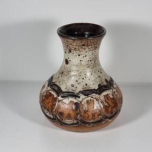 May include: A small, white ceramic vase with brown speckles and a brown rim. The vase has a rounded body with a raised, textured design of brown circles.