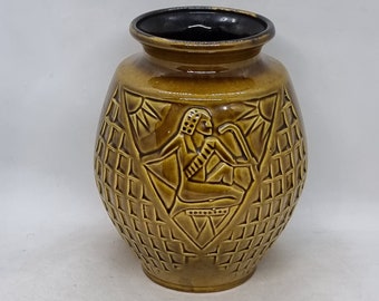 May include: A brown ceramic vase with a geometric pattern and a raised image of a person in a seated position. The vase has a black rim.