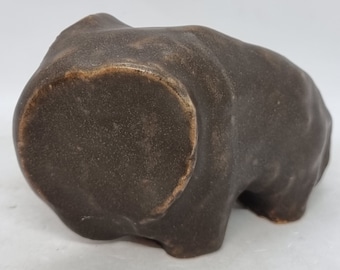 May include: A dark brown ceramic sculpture of a crouching animal. The sculpture has a rough, textured surface and is shaped like a bear or a dog.