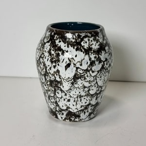 以下が含まれることがあります： 茶色と白の斑点模様が施された、小さな白い陶器の花瓶。花瓶の縁は濃い青色です。