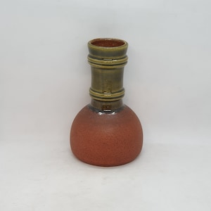 Könnte beinhalten: Eine braune und grüne Keramikvase mit abgerundetem Boden und zylindrischem Hals. Die Vase hat eine strukturierte Oberfläche und eine glänzende Oberfläche.