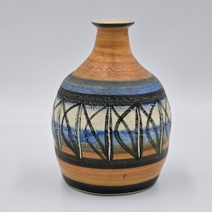 May include: A ceramic vase with a textured, orange-brown body and a narrow neck. The vase features a band of blue and black geometric patterns, with a black base. The vase is approximately 20 cm tall.