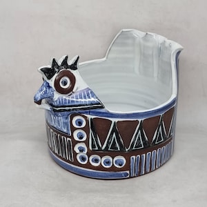 以下が含まれることがあります： 青、茶色、白の幾何学模様が施された、スタイリッシュな鶏の形をしたセラミック製のプランター。プランターは上部に大きな開口部があり、側面に小さな注ぎ口があります。