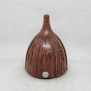 May include: A brown ceramic vase with a textured, wood-like design. The vase has a narrow neck and a wide, flared base. The bottom of the vase has a blue and white label that reads "Handcrafted Ceramic".
