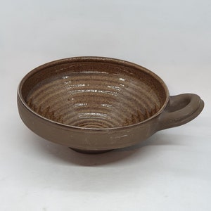 May include: A brown ceramic bowl with a textured, swirling pattern inside. The bowl has a single handle on the side.