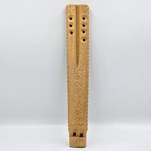 May include: A light brown, elongated wooden flute featuring intricate hand-carved geometric patterns along its length. The instrument has two parallel rows of finger holes and a central channel, with decorative notched edges running down both sides.