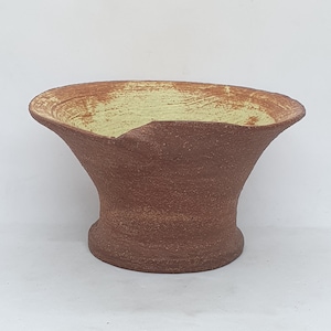 May include: A brown ceramic vase with a wide, flared opening and a yellow glaze. The vase has a rough, textured surface and a slightly uneven rim.