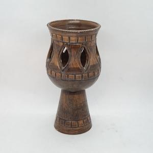 May include: A brown ceramic planter with a decorative design and cut-out details. The planter has a wide base and a narrow top.