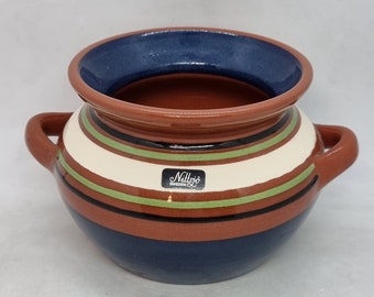 May include: A ceramic pot with a dark blue interior and rim, featuring horizontal stripes in cream, green, and black. The pot has two handles and a label that reads "Nittsjö Sweden". The exterior is primarily brown and dark blue.