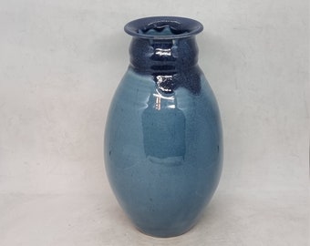 May include: A blue ceramic vase with a dark blue rim. The vase has a rounded body and a narrow neck.