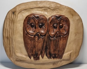 Könnte beinhalten: Eine Keramik-Wandplatte mit zwei braunen Eulen mit großen Augen, die auf einem Ast sitzen. Die Platte ist hellbraun und hat eine strukturierte Oberfläche.