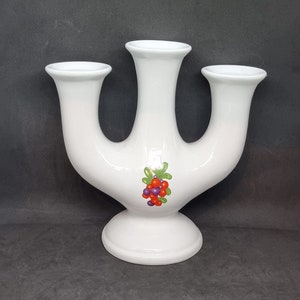 Op de afbeelding: Witte keramische kandelaar met drie armen en een bloemmotief met rode en paarse bessen.