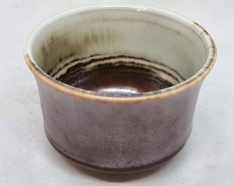 May include: A small, round ceramic bowl with a brown and white striped design. The bowl has a white interior and a brown exterior.