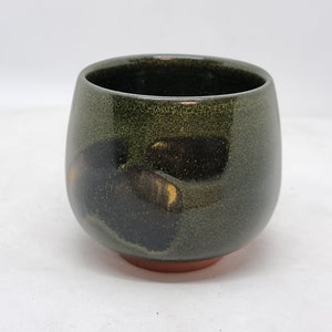 Puede incluir: Un cuenco de cerámica hecho a mano con un esmalte verde oscuro y una base marrón rojizo. El cuenco tiene una forma redondeada y un acabado liso y brillante. El interior del cuenco es oscuro, con toques dorados. Ideal para sopas o postres.