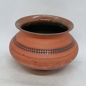 Puede incluir: Una pequeña maceta de terracota con un esmalte marrón y un patrón decorativo alrededor del borde. La maceta está vacía y tiene una forma ligeramente redondeada.