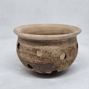 May include: A small, brown terracotta planter with drainage holes and a painted floral design. The planter is ideal for small plants or succulents.
