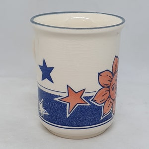 Puede incluir: Taza de cer&aacute;mica blanca con un dise&ntilde;o floral azul y naranja. El dise&ntilde;o presenta estrellas y flores.