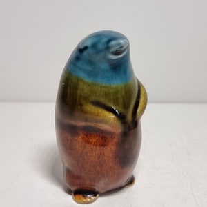 Puede incluir: Una figurita de cerámica de un pingüino con un esmalte azul, verde y marrón. El pingüino está de pie con las alas plegadas.