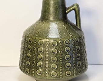 Può includere: Un vaso in ceramica verde con un motivo circolare testurizzato e un'unica maniglia. Il vaso ha una base larga e un collo stretto.