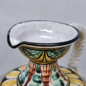 May include: A ceramic pitcher with a white glaze and a black rim. The pitcher has a floral design with yellow, green, and red accents. The pitcher has a spout and a handle.