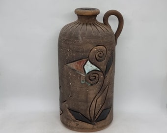 Peut inclure: Un vase en céramique brun avec un motif de fleur stylisé en noir, blanc et bleu. Le vase a une anse et une surface texturée.