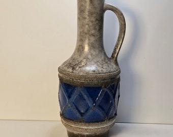 Könnte beinhalten: Eine Keramikvase mit grauer und blauer Glasur. Die Vase hat einen breiten Boden und einen schmalen Hals mit einem Henkel. Der Boden der Vase ist mit einem blauen Diamantenmuster verziert.