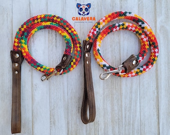 May include: Two colorful dog leashes with a brown leather handle. The leashes are made of braided rope with red, orange, yellow, green, and white stripes. The leashes are on a white wooden background. "CALAVERA Handmade for Pets" is written in orange on a white background.