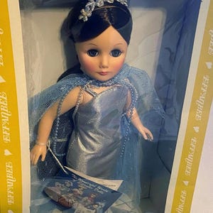 May include: A porcelain doll wearing a light blue gown and a crown. The doll has dark hair and blue eyes. The doll is in a box with the words "Effanbee" printed on it.
