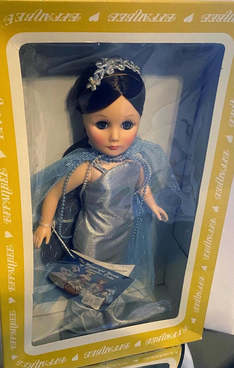 May include: A porcelain doll wearing a light blue gown and a crown. The doll has dark hair and blue eyes. The doll is in a box with the words "Effanbee" printed on it.