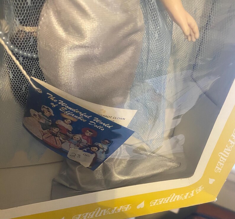 May include: A silver and blue doll wearing a long, flowing gown with a tulle overlay. The doll is part of "The Wonderful World of Eibabie Dolls" collection. The doll is packaged in a yellow box with a heart design.