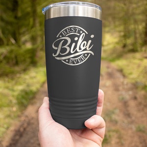 May include: A dark gray stainless steel tumbler with a white inscription that reads "Best Bibi Ever" in a circle with stars.