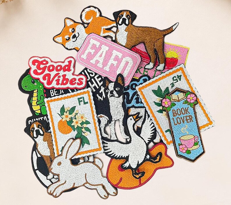 May include: A collection of embroidered patches featuring various designs including a white rabbit, a goose, a green dinosaur, a Boston Terrier, a brown dog, an orange fruit branch, a book lover sign with a teacup, and text reading FAFO and Good Vibes.