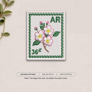 May include: A rectangular embroidered patch designed like a postage stamp with a white background and a green scalloped border. It features a branch with pink and white flowers, green leaves, the letters AR, and the text 36 cents in green thread.