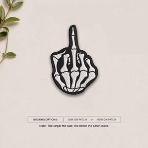May include: An embroidered patch featuring a white skeleton hand making a middle finger gesture with black outlines and details. The text below reads: BACKING OPTIONS: SEW ON PATCH or IRON ON PATCH. Note: The larger the size, the better the patch looks.