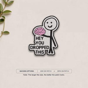 May include: An embroidered patch featuring a black stick figure holding a pink brain. The text HEY YOU DROPPED THIS is stitched in black below the brain. The patch has a white background and a black border. Below the patch, text reads BACKING OPTIONS: SEW ON PATCH or IRON ON PATCH. Note: The larger the size, the better the patch looks.