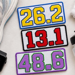 May include: Three rectangular embroidered patches featuring marathon distances. The top patch displays 26.2 in yellow with a blue border. The middle patch shows 13.1 in red with a black border. The bottom patch features 48.6 in purple with a green border.