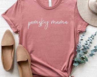 Könnte beinhalten: Ein staubiges rosafarbenes T-Shirt mit dem Text "pomsky mama" in weißen Buchstaben.