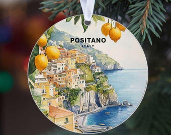 May include: Round Christmas ornament featuring a watercolor painting of Positano, Italy. The image shows colorful buildings on a cliffside, the sea, and lemons. The text "POSITANO ITALY" is at the top. A white ribbon is attached.