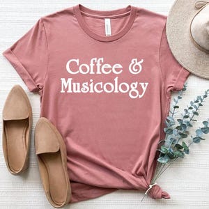May include: A dusty rose t-shirt with the text "Coffee & Musicology" printed in white.