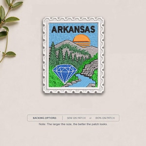 May include: A rectangular embroidered patch shaped like a postage stamp featuring the word ARKANSAS in black text. The design depicts a mountain landscape with green pine trees, a blue diamond, a winding river, and an orange sun against a blue sky.